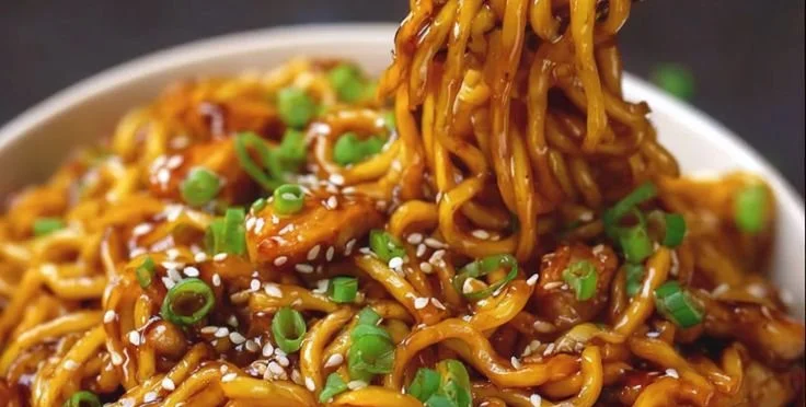 Plate of sticky garlic chicken noodles garnished with green onions.